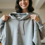 A person holding a soft, well-maintained gray hoodie with a content expression