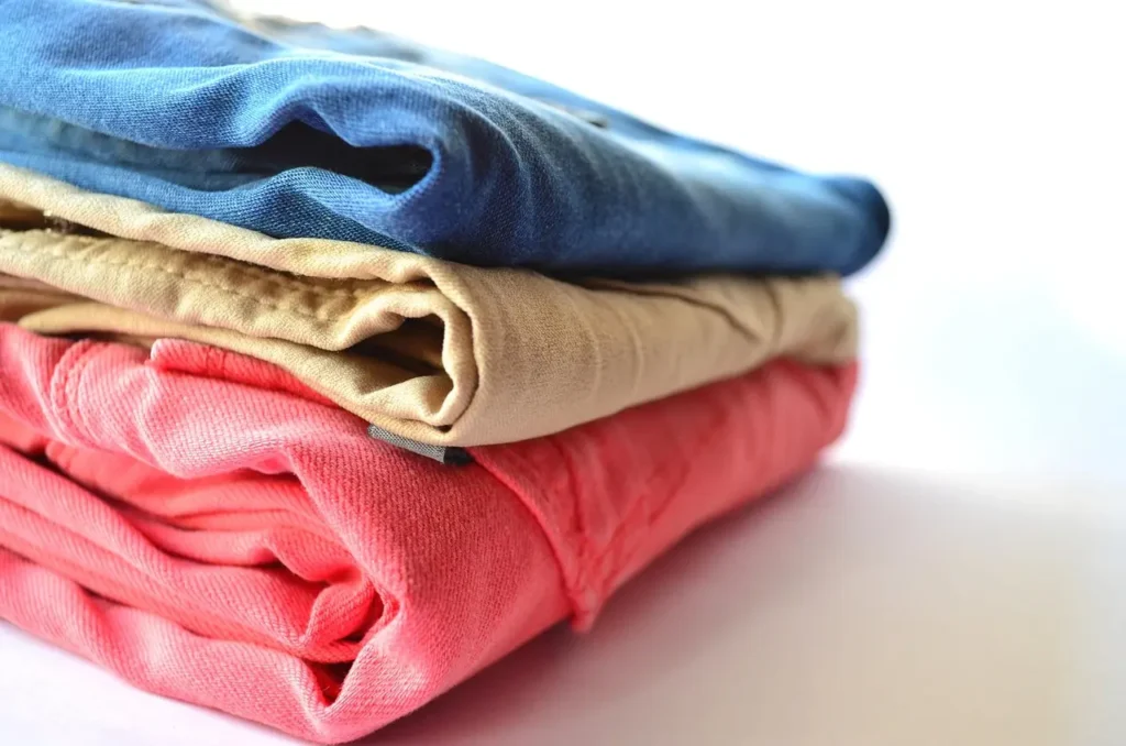 A neatly folded stack of colorful t-shirts on a wooden shelf